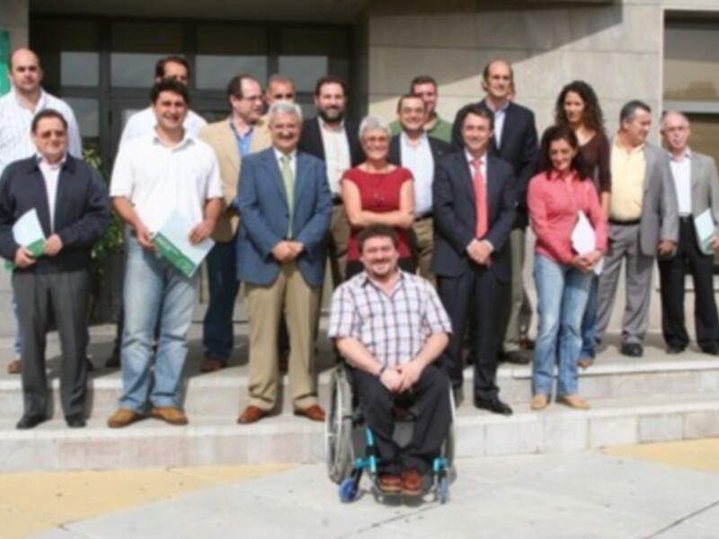 Una reunión de trabajo con varias personas, incluyendo a un hombre en silla de ruedas, posando para una foto frente a una construcción.