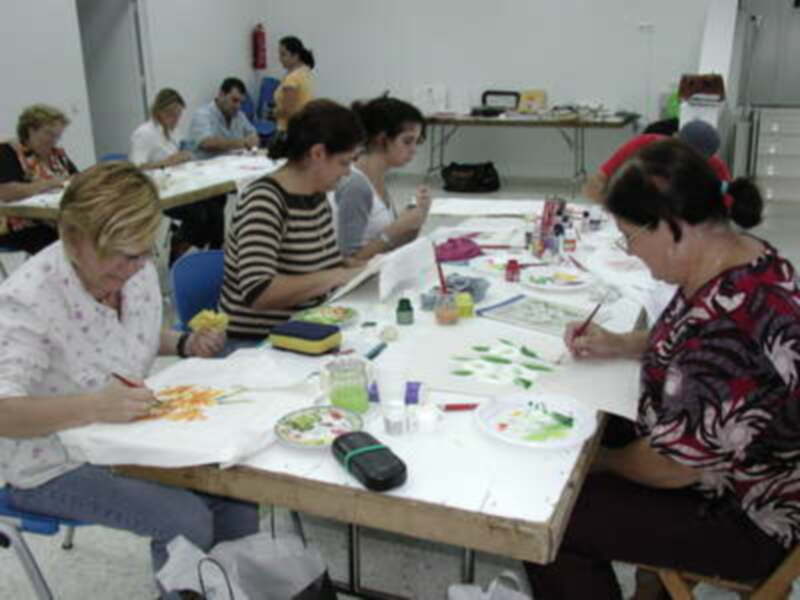 Clase de pintura en un taller. Personas trabajando con pinceles y colores sobre papel. Ambiente creativo y enriquecedor.