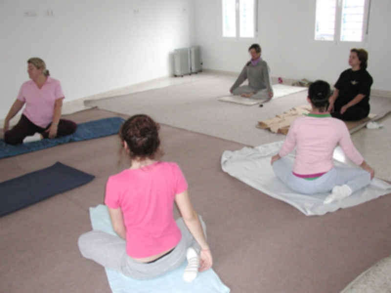 Un grupo de personas meditando en una habitación con colchones y estantes.