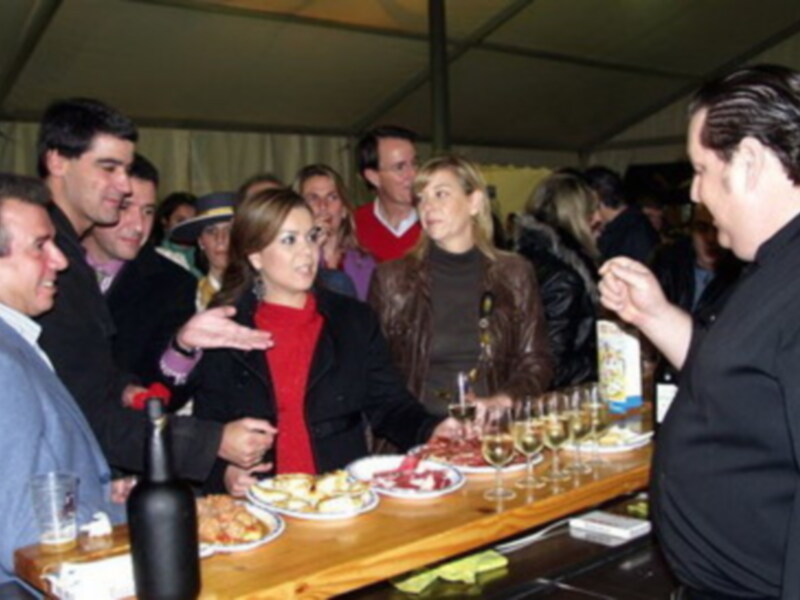 Personas reunidas en una mesa con bebidas y comida, bajo un toldo.