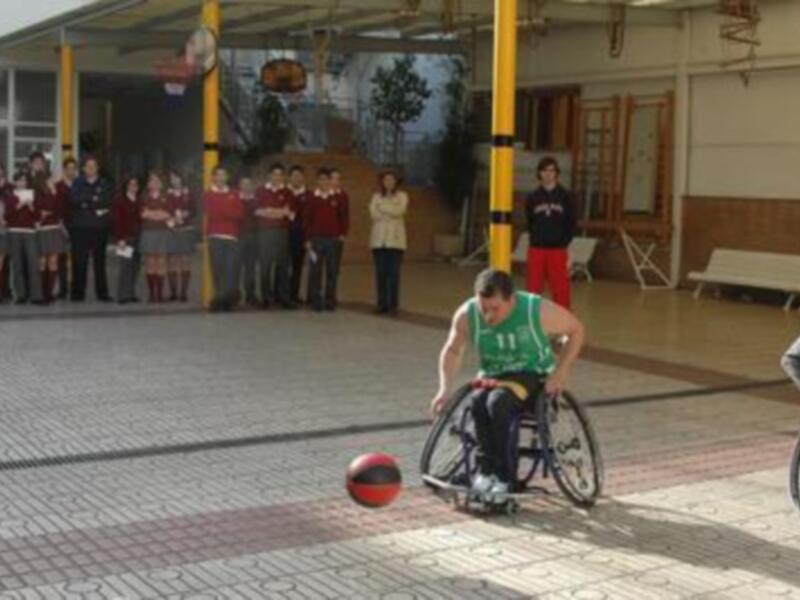 Un hombre en silla de ruedas juega baloncesto en una cancha de baloncesto dentro de un gimnasio.