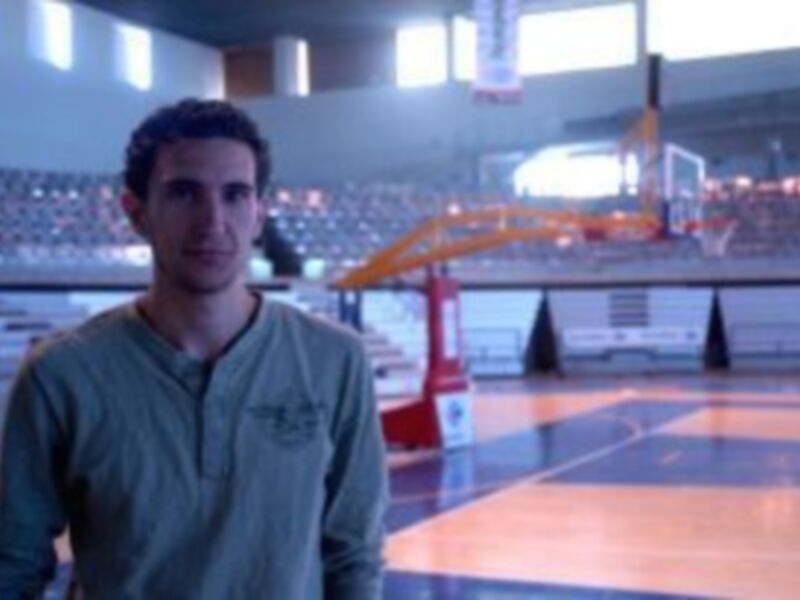 Persona joven en una cancha de baloncesto, con gradas vacías al fondo.