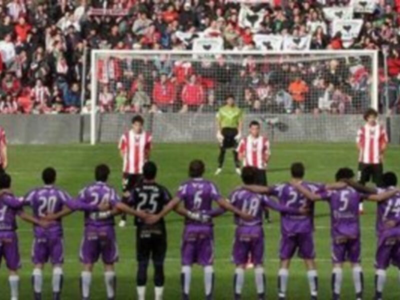 Equipo de fútbol en uniforme púrpura haciendo un minuto de silencio antes del partido.