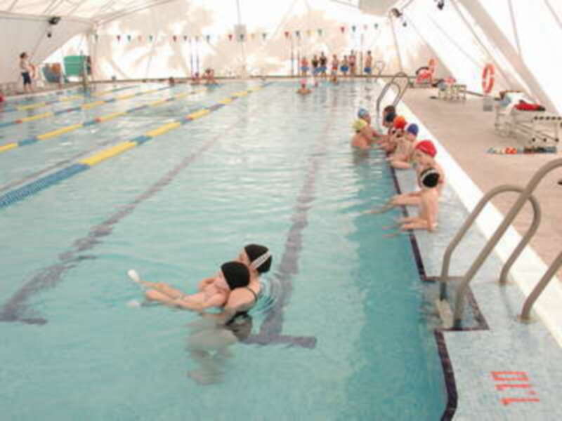 Niños aprendiendo a nadar en una piscina interior con azulejos azules y amarillos en las paredes.