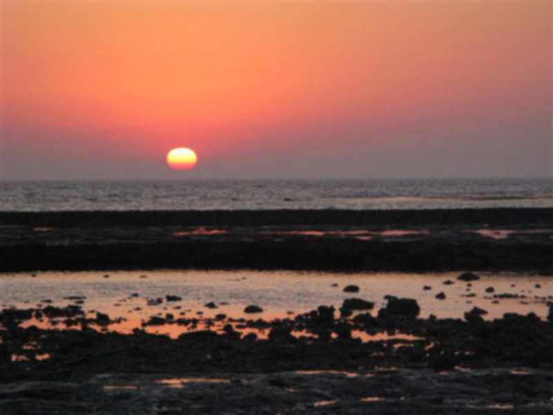Puesta de sol sobre el mar, con un cielo rojizo y una pila de arena en primer plano.
