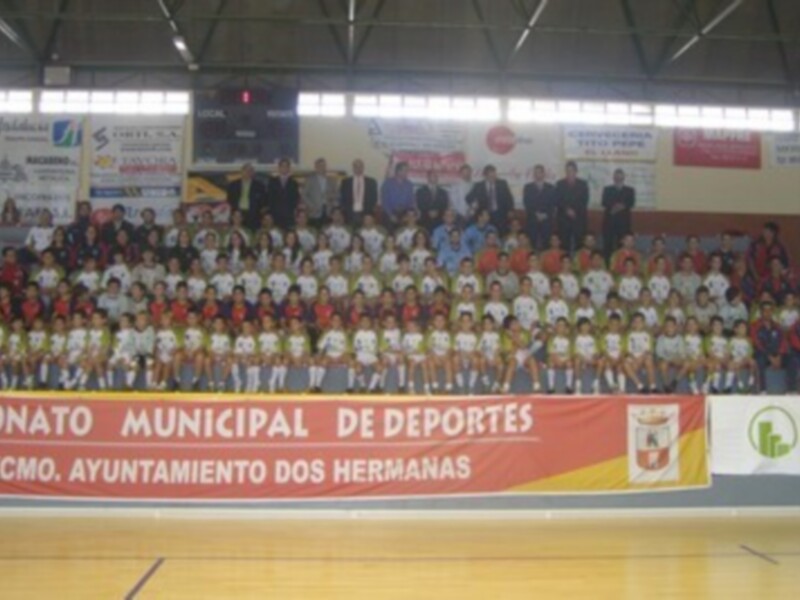 Equipo de fútbol en una cancha de fútbol, con público en el estadio. Anuncio de torneo municipal de deportes en el fondo.