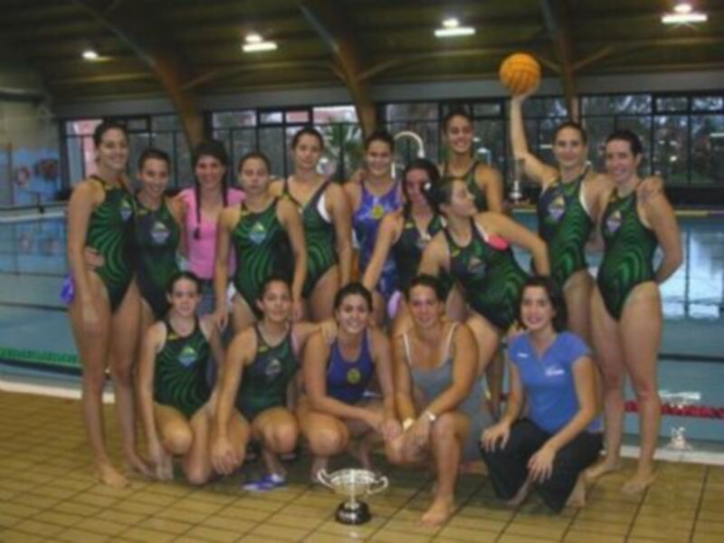 Equipo de waterpolo celebrando con el trofeo en una piscina.