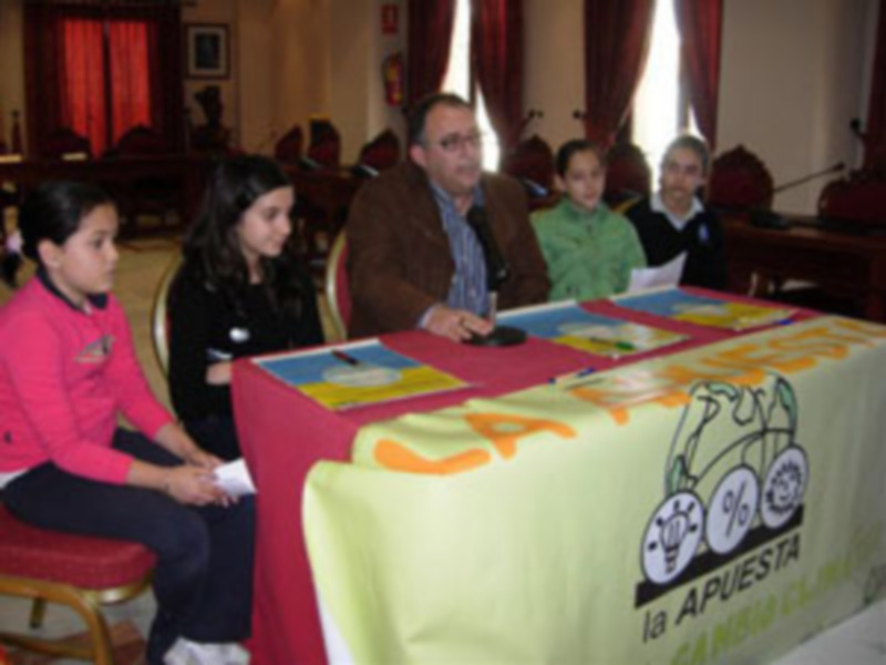Una familia está sentada en una mesa con un cartel que dice "Apuesta". La imagen muestra a adultos y niños, posiblemente en una reunión o evento familiar.