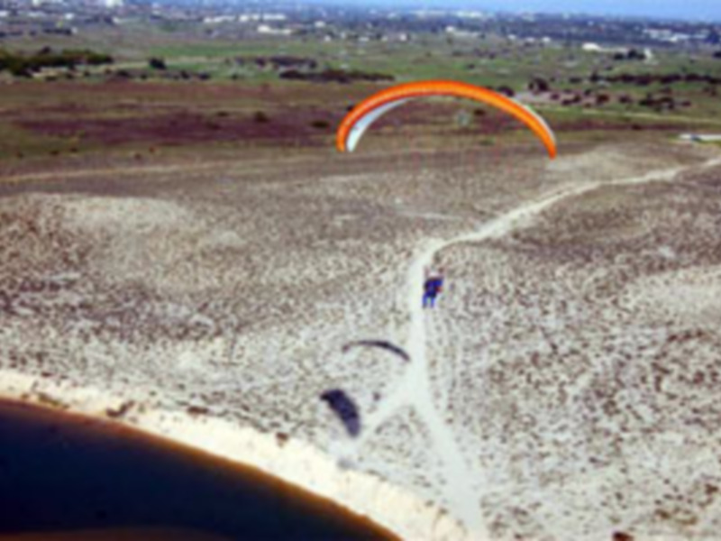 Parasailing over a sandy beach with a clear blue sky and distant hills.