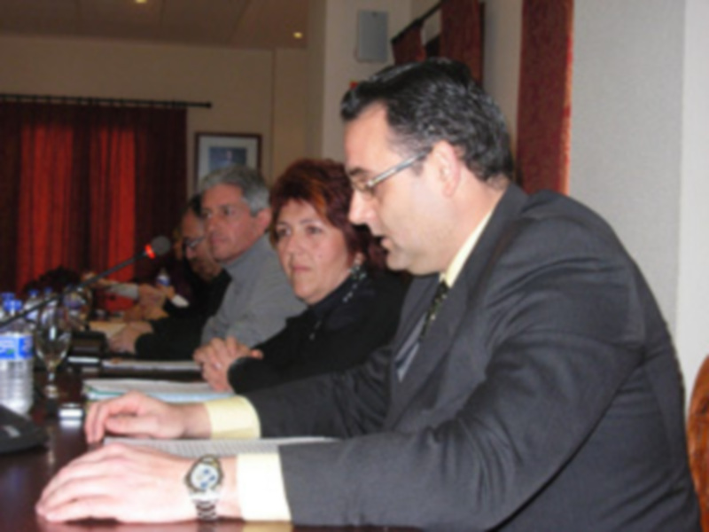 Un hombre en una reunión de negocios, sosteniendo un documento mientras otros asisten al fondo.