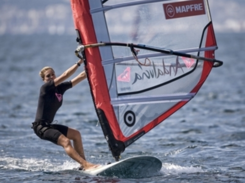 Un windsurfer disfruta de un día de viento fuerte en el mar, controlando su barco con una vela Mapfre.