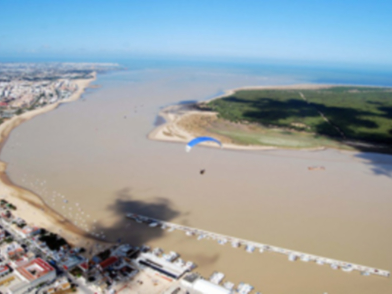 Vista aérea de una bahía con parapente en el cielo y edificios al borde del agua.