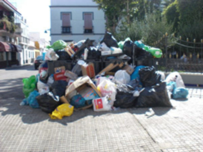 Un montón de basura en la calle, incluyendo bolsas de plástico y papel, con edificios al fondo.