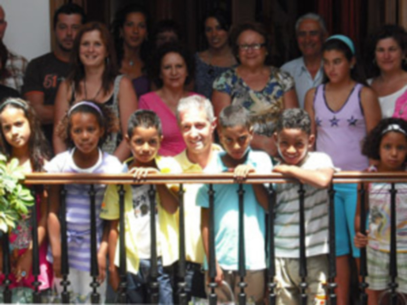Una familia multigeneracional se toma una foto en un balcón, con adultos y niños sonriendo. La imagen muestra una diversidad de edades y estilos, reflejando la unidad familiar.