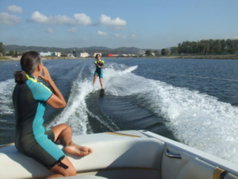 Dos personas disfrutan de una aventura de remolque náutico en un lago, con el sol brillando en un cielo azul.