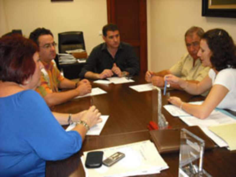 Reunión de trabajo en una oficina, personas discutiendo alrededor de una mesa llena de documentos y teléfonos móviles.