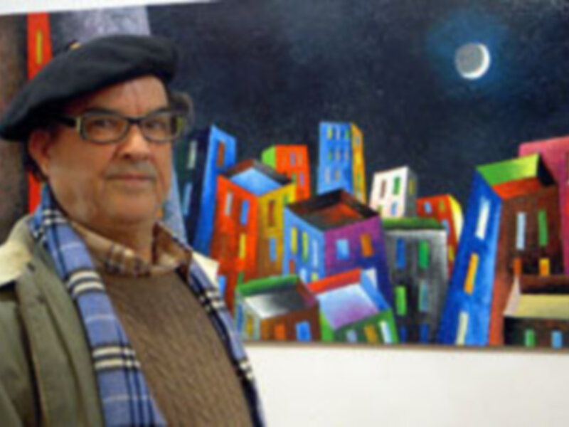 Un hombre con una gorra y bufanda posa frente a un cuadro de pintura que muestra una ciudad nocturna con edificios coloridos bajo una luna brillante.