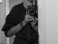 Una persona con una camisa negra y una cámara en la mano, posando frente a un espejo en blanco y negro.