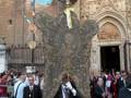 Un hombre en traje negro con un sombrero de copa lleva una vara roja, frente a la catedral de Segovia. La imagen muestra una procesión religiosa con personas vestidas formalmente, incluyendo un hombre en traje negro y sombrero de copa. La catedral, con su arquitectura gótica, se ve en el fondo.