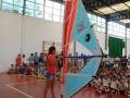 Una niña enseñando a niños en una cancha de voleibol, con un modelo de vela en la mano.