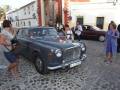 Vintage car on cobblestone street, surrounded by people and historic buildings.
