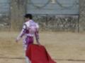 Un torero en traje de luces con capa roja, preparándose para el toreo en una plaza de toros.