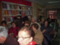 Un grupo de personas en una sala llena de libros, posiblemente en un evento o conferencia. La imagen muestra a varias personas sentadas y otros que están caminando por la sala, con estanterías llenas de libros en el fondo.