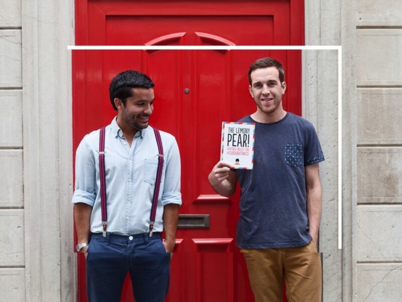 Dos hombres sonrientes frente a una puerta roja, uno sostiene un libro titulado "The Element of Fear".