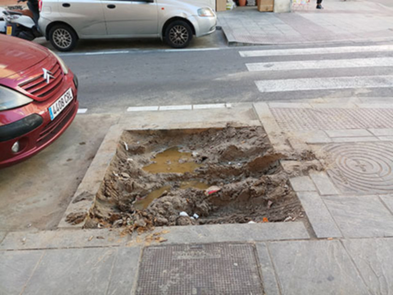 Un agujero en la calle con tierra y basura, cerca de un semáforo.