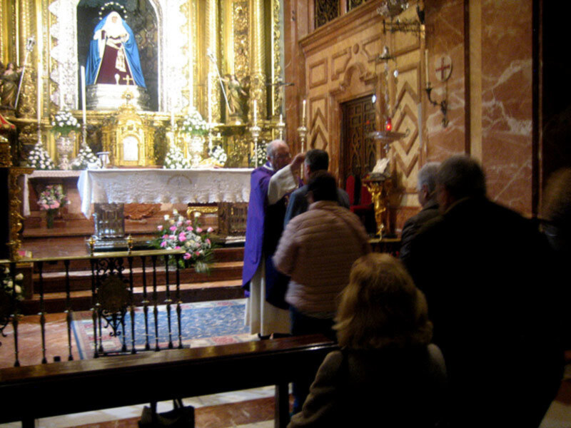 Interior de una iglesia con altares ornamentados y personas participando en una ceremonia religiosa.