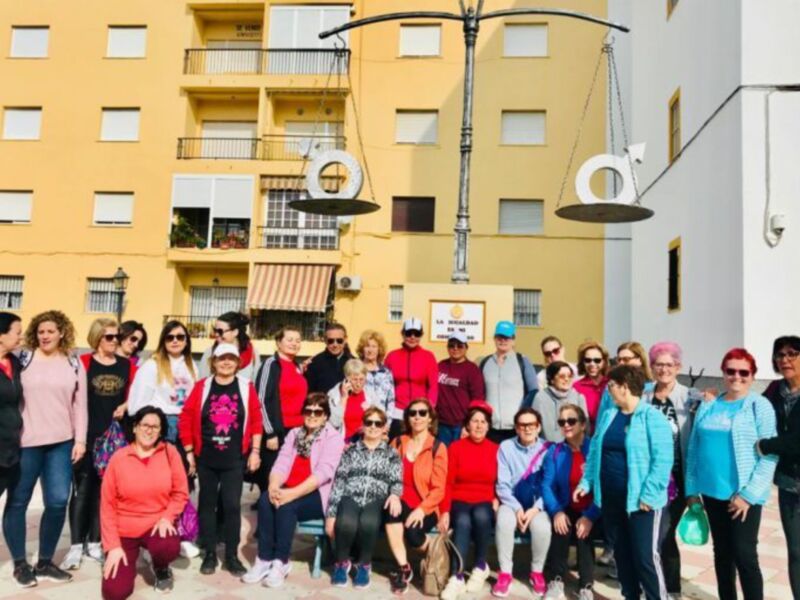 Gruppo di donne in posa per una foto di gruppo in una piazza urbana con un edificio residenziale dietro di loro.