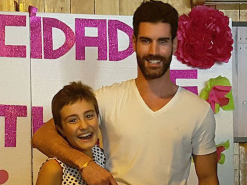 Dos personas sonrientes frente a un fondo con letras y flores.