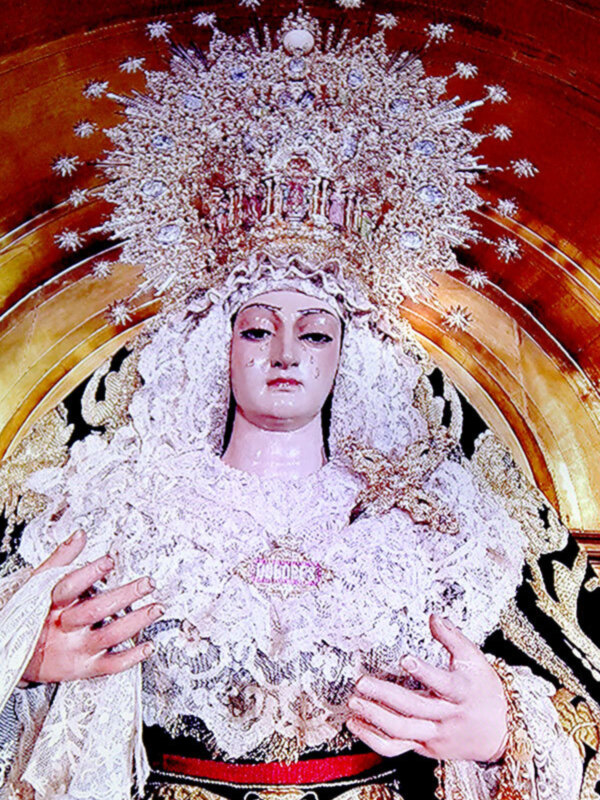 Imagen de la Virgen María vestida con un manto blanco y una corona de estrellas, posiblemente en un altar o iglesia.