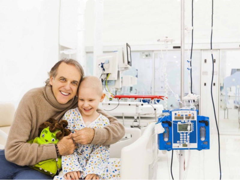 Un niño con cáncer sonríe con su padre en un hospital, rodeados de tecnología médica.