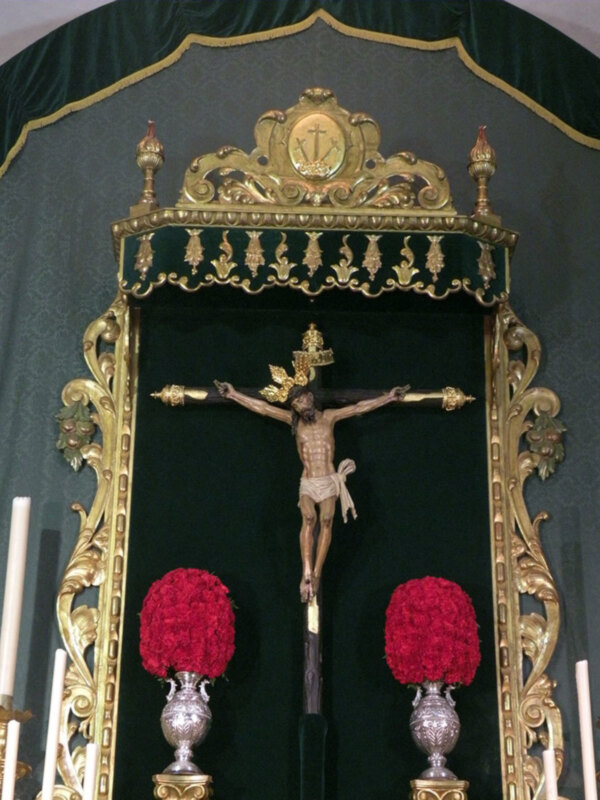 Imagen de una cruz en un altar con detalles dorados y rojos.
