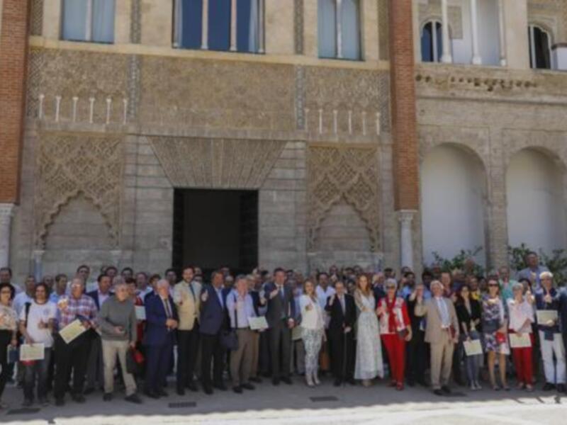 Una gran cantidad de personas posan juntas en frente de un edificio histórico, todos sostienen diplomas y sonríen para la foto. El edificio tiene una arquitectura clásica con columnas y ventanas altas.