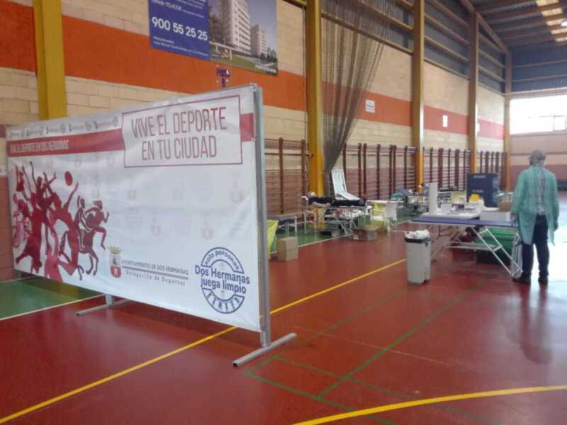 Salón de deportes con piso rojo y verde, banner promocional del programa "Vive el Deporte en tu Ciudad", y una persona caminando con un carrito de compras.