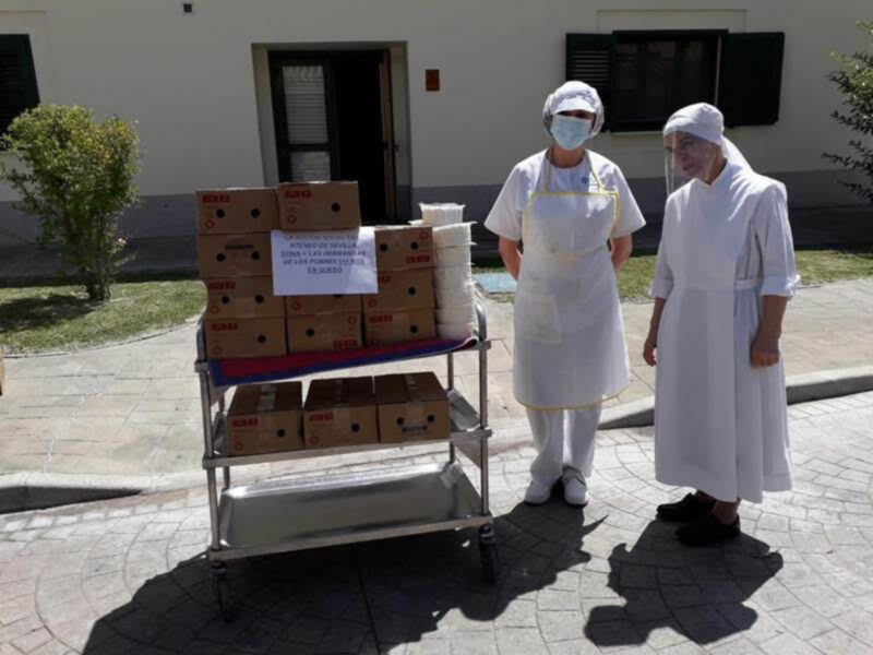 Dos personas vestidas con uniformes de trabajo están frente a una carrito lleno de cajas y rollos de papel. La escena parece ser en un entorno urbano, con una puerta y ventanas al fondo.
