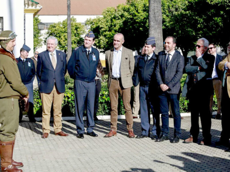 Una imagen de varias personas en uniforme militar y civiles, posiblemente oficiales o militares, en un entorno urbano con árboles y edificios al fondo. La escena parece ser formal o ceremonial, posiblemente en un evento oficial o de celebración.