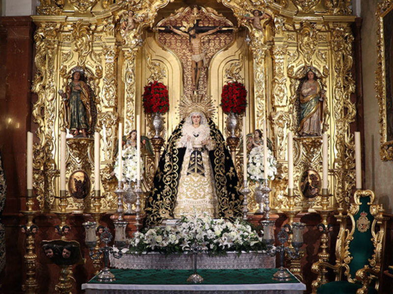 Altar dorado con estatuas religiosas y flores blancas.