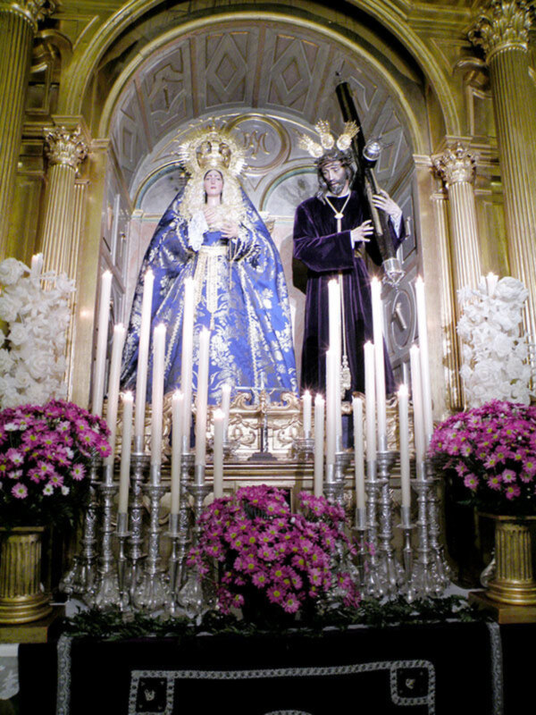 Estátuas religiosas en un altar con flores y velas, decoración dorada.