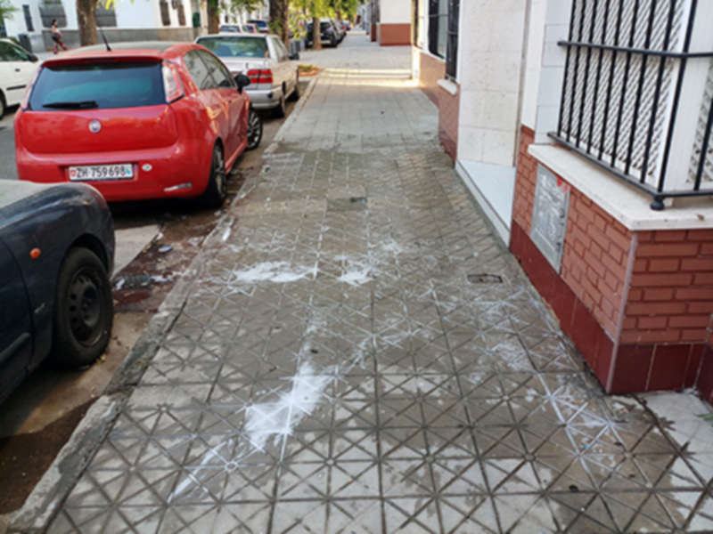 Pavimento con patrón geométrico y coches aparcados en una calle urbana.