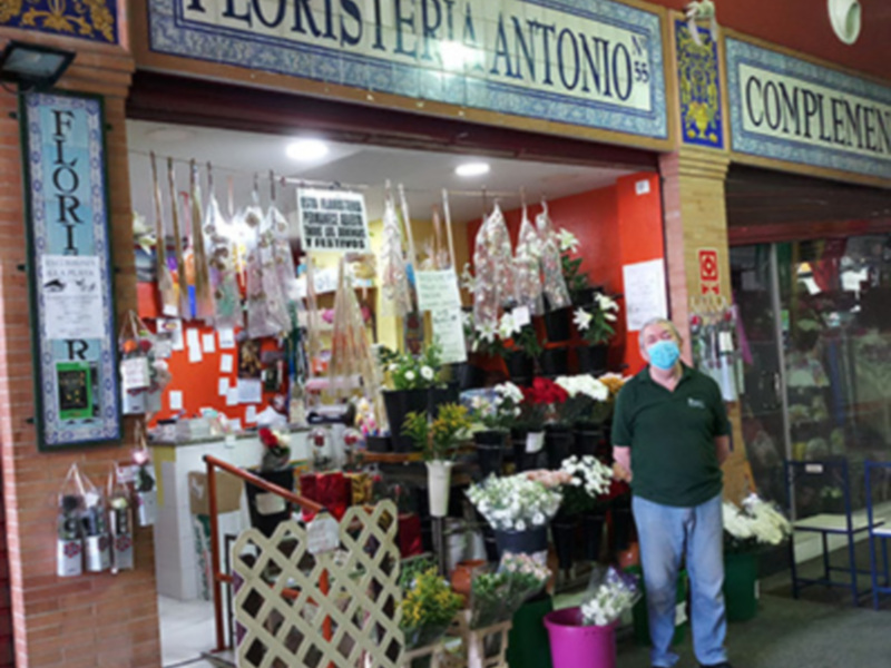 Persona con mascarilla frente a Floristería Antonio, con variedad de flores y decoraciones en el interior.