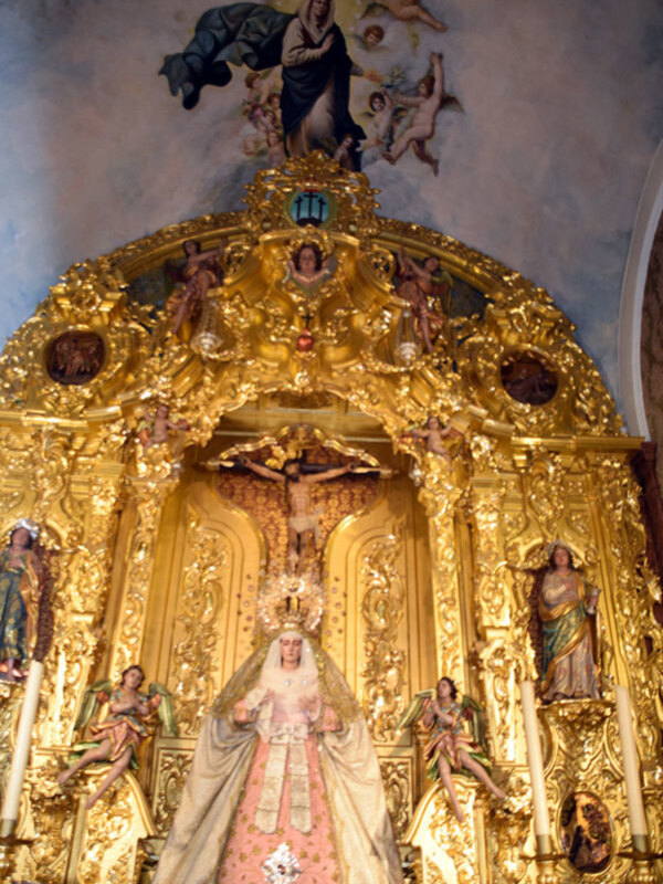 Altar de oro con estatuas de la Virgen María y santos, rodeado de flores y velas.