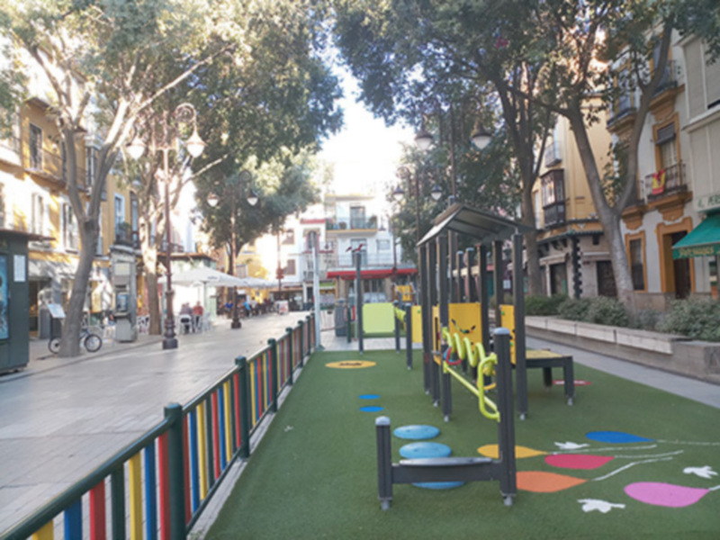 Jardín infantil en la calle, con juegos de colores y árboles.