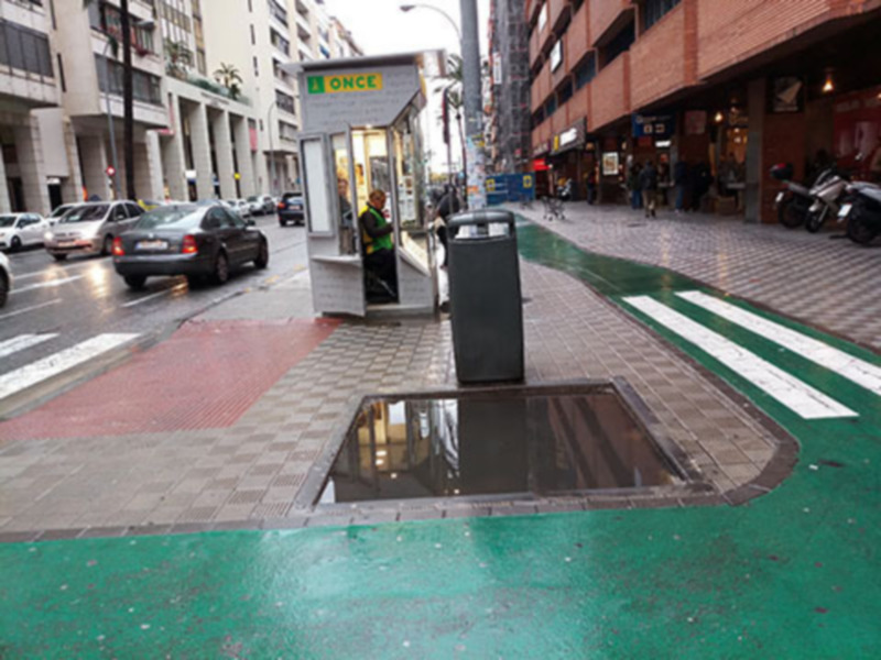 Caja de seguridad de la ONCE en una calle urbana con peatonal y vehículos al fondo.