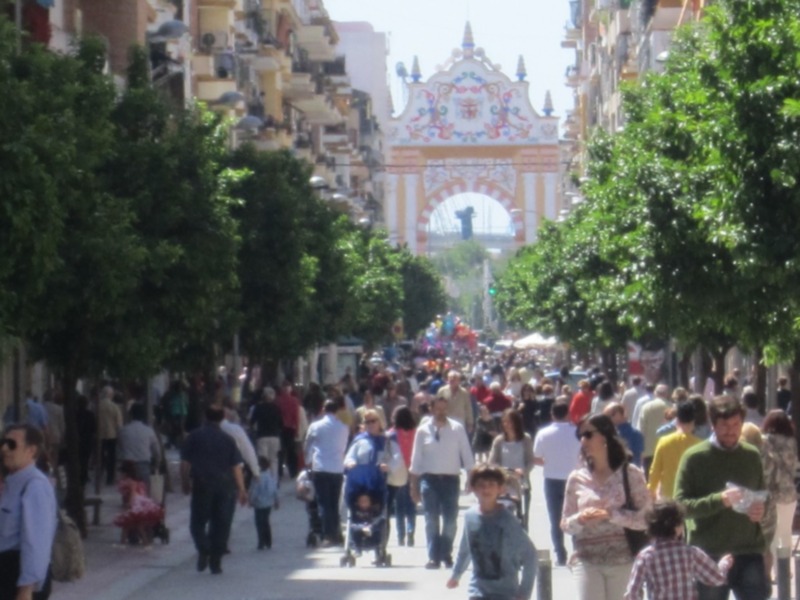 Una calle con edificios históricos y arcos, gente caminando bajo un cielo claro.