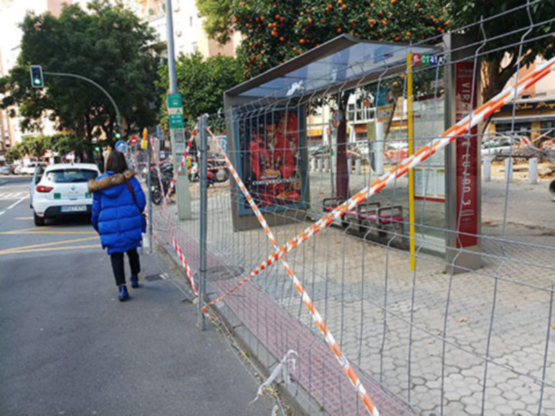 Pié de foto: Una mujer camina por una calle con un coche blanco y negro a su lado. Hay una señal de tráfico en el poste, una valla de seguridad con cinta roja y amarilla, y un parque infantil en el fondo.