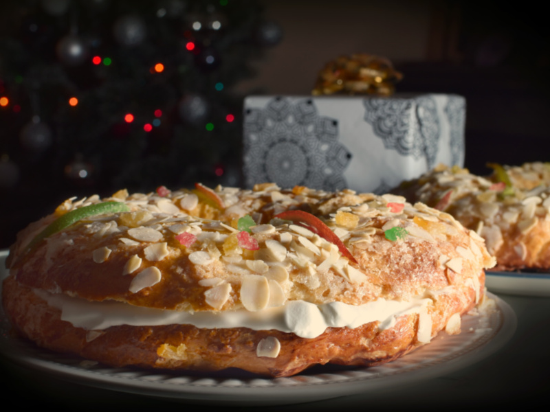 Pastel de Navidad con crema y frutas secas, sobre un plato blanco. Fondo borroso con luces navideñas y una caja de regalo.