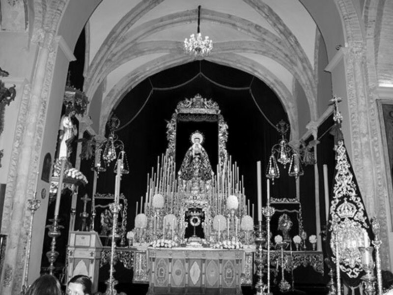Interior de una iglesia con altar ornado y alta imagen de la Virgen María en un retablo, en blanco y negro.